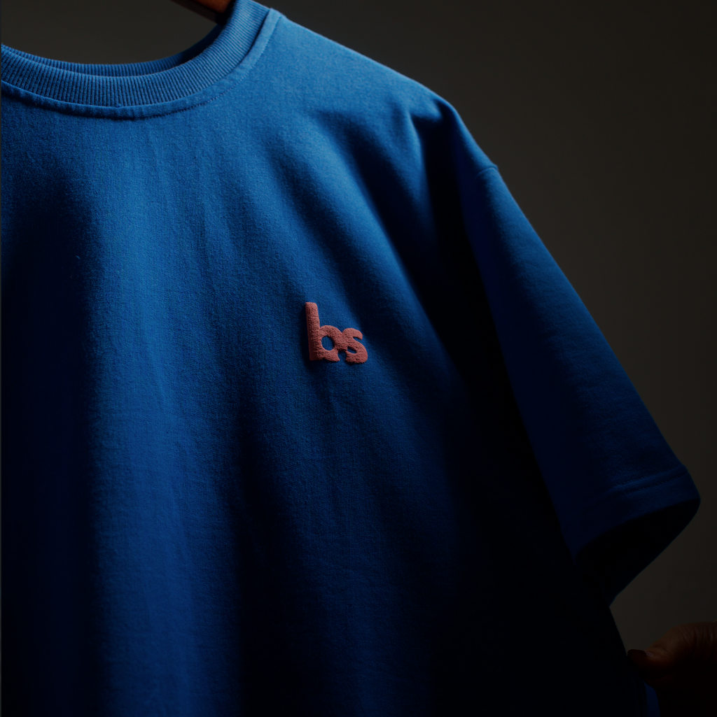 Blue t-shirt with a logo on a hanger against a dark background
