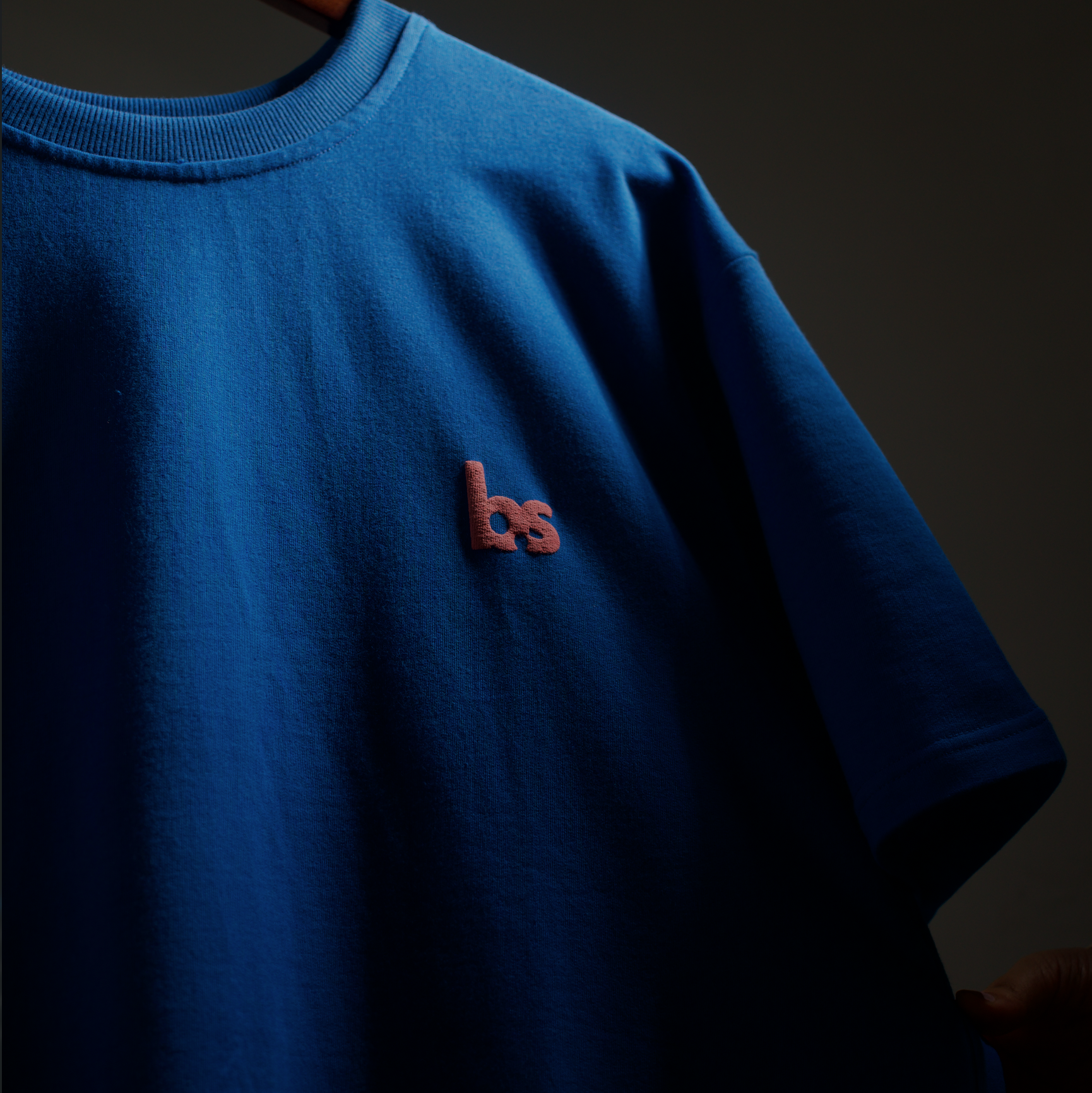 Blue t-shirt with a logo on a hanger against a dark background
