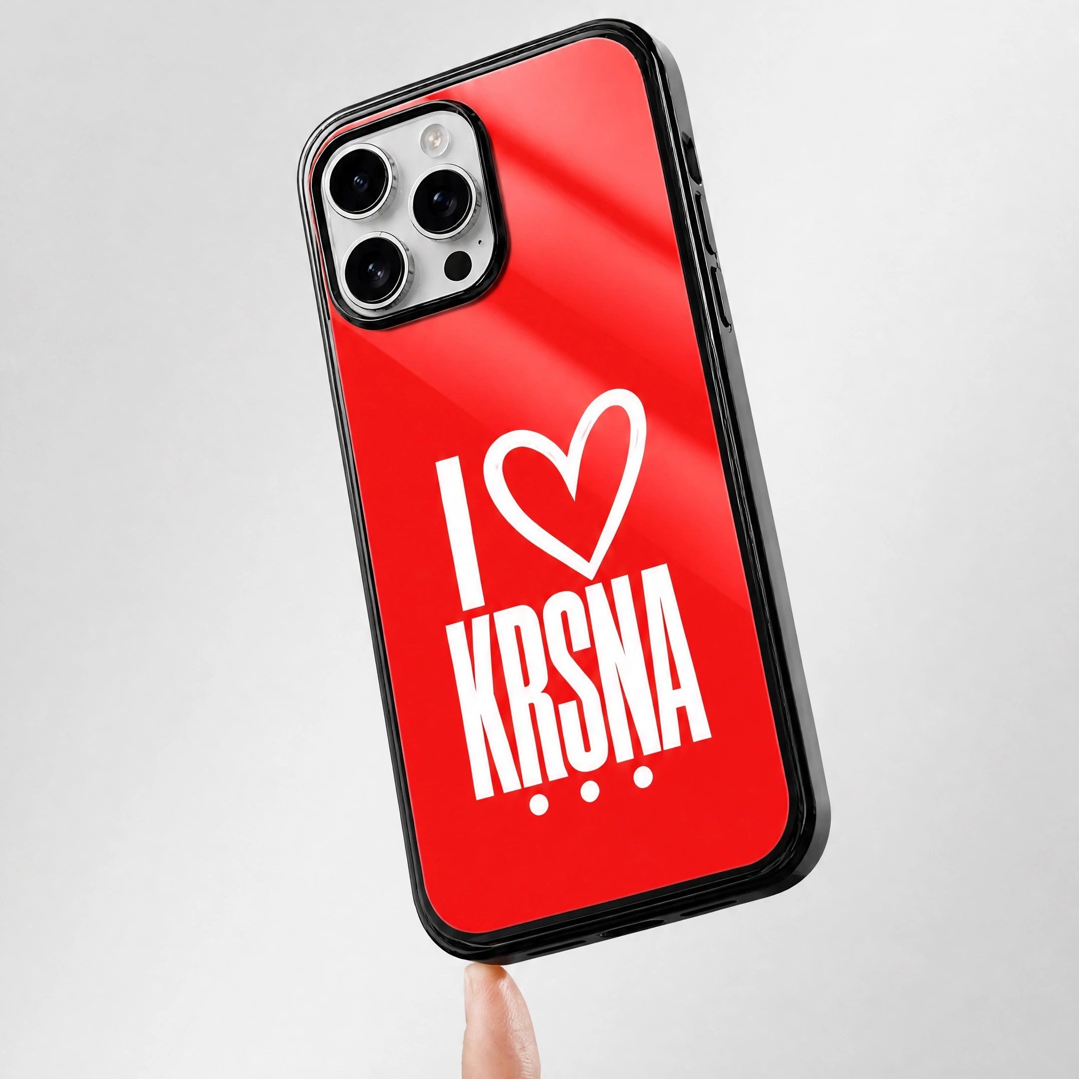 Phone case with 'I ❤️ Krsna' text on a red background, held by a finger.